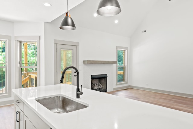 kitchen featuring lofted ceiling, white cabinets, sink, hanging light fixtures, and light hardwood / wood-style flooring