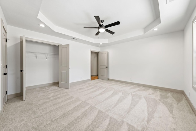 unfurnished bedroom featuring ceiling fan, a raised ceiling, light colored carpet, and a closet