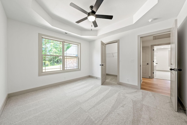 unfurnished bedroom with light carpet, a raised ceiling, ceiling fan, a spacious closet, and a closet