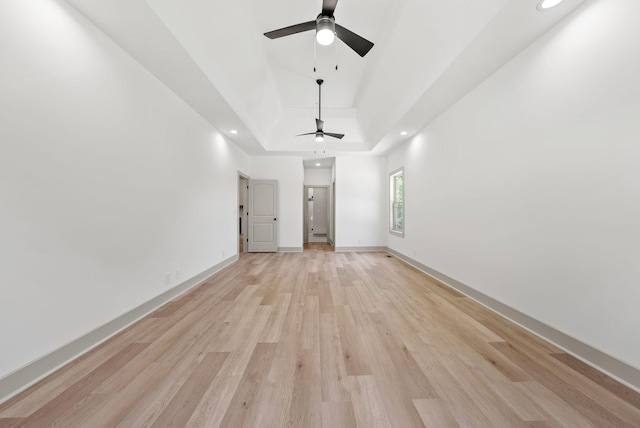 unfurnished living room featuring ceiling fan, a tray ceiling, and light hardwood / wood-style flooring