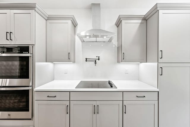 kitchen featuring decorative backsplash, wall chimney exhaust hood, stainless steel double oven, black electric cooktop, and gray cabinets