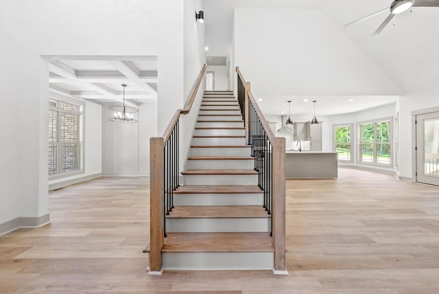 stairs featuring a high ceiling, coffered ceiling, wood-type flooring, and ceiling fan with notable chandelier