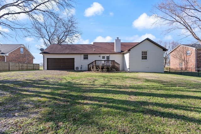 rear view of house featuring a garage, a deck, and a lawn