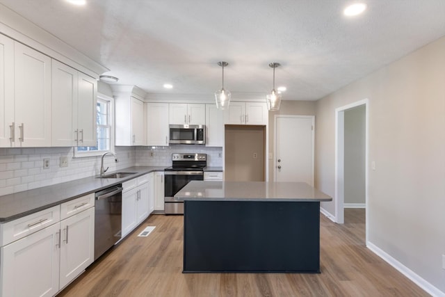 kitchen with appliances with stainless steel finishes, sink, pendant lighting, white cabinets, and a center island