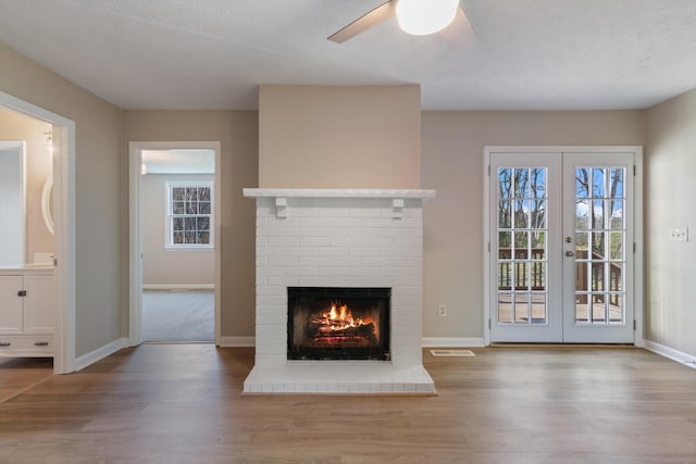 unfurnished living room with french doors, light hardwood / wood-style flooring, a brick fireplace, and ceiling fan