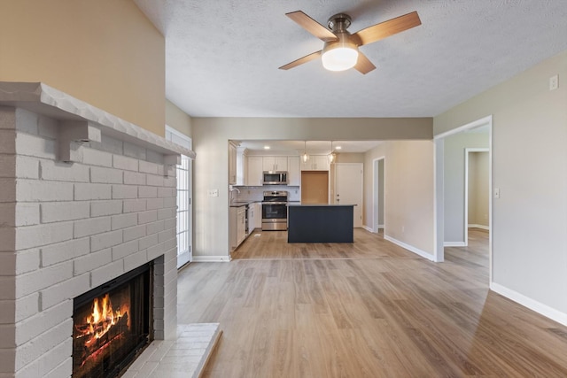 unfurnished living room with a textured ceiling, ceiling fan, light hardwood / wood-style flooring, and a brick fireplace