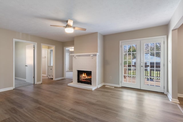 unfurnished living room with ceiling fan, french doors, wood-type flooring, a textured ceiling, and a fireplace