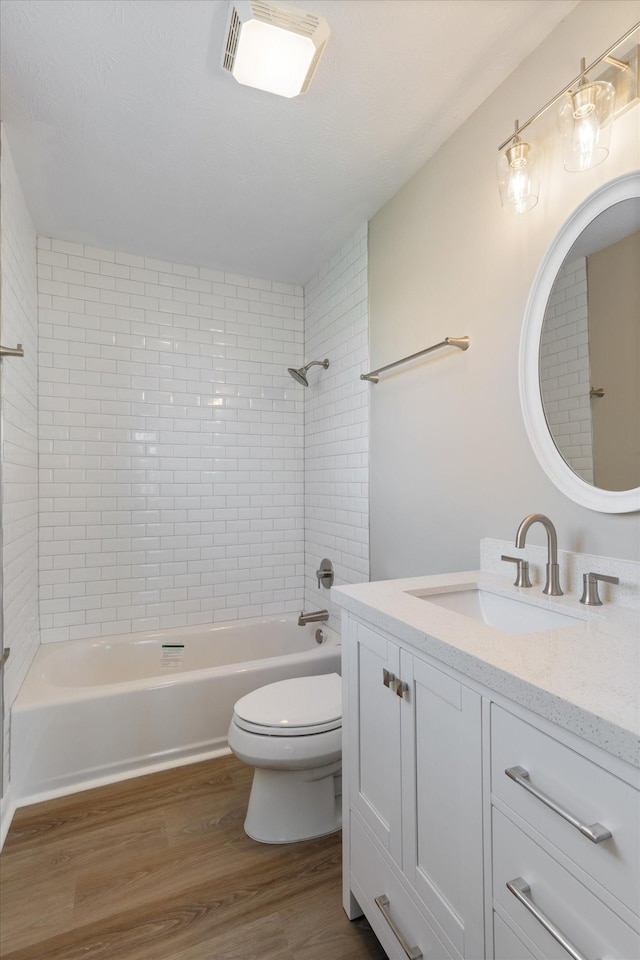 full bathroom featuring vanity, wood-type flooring, tiled shower / bath combo, and toilet