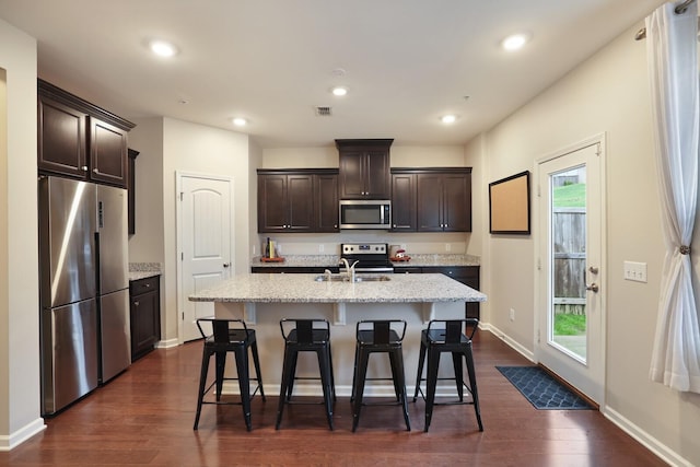 kitchen featuring a breakfast bar, appliances with stainless steel finishes, dark hardwood / wood-style floors, and a kitchen island with sink