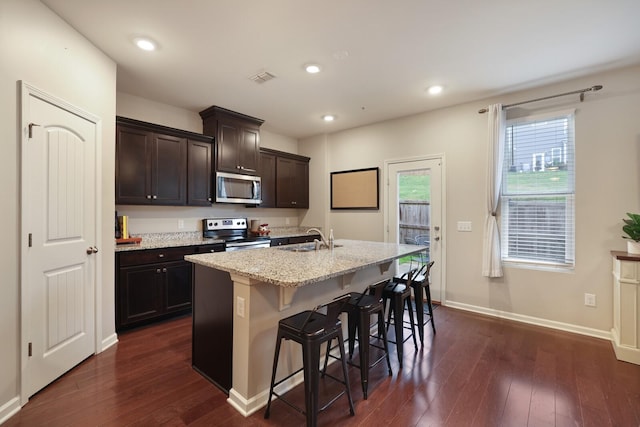 kitchen featuring sink, stainless steel appliances, dark hardwood / wood-style flooring, a kitchen bar, and a center island with sink