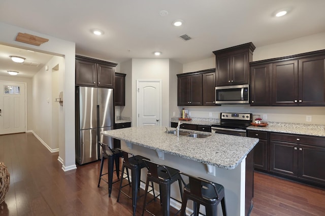 kitchen with appliances with stainless steel finishes, dark hardwood / wood-style flooring, light stone counters, and sink