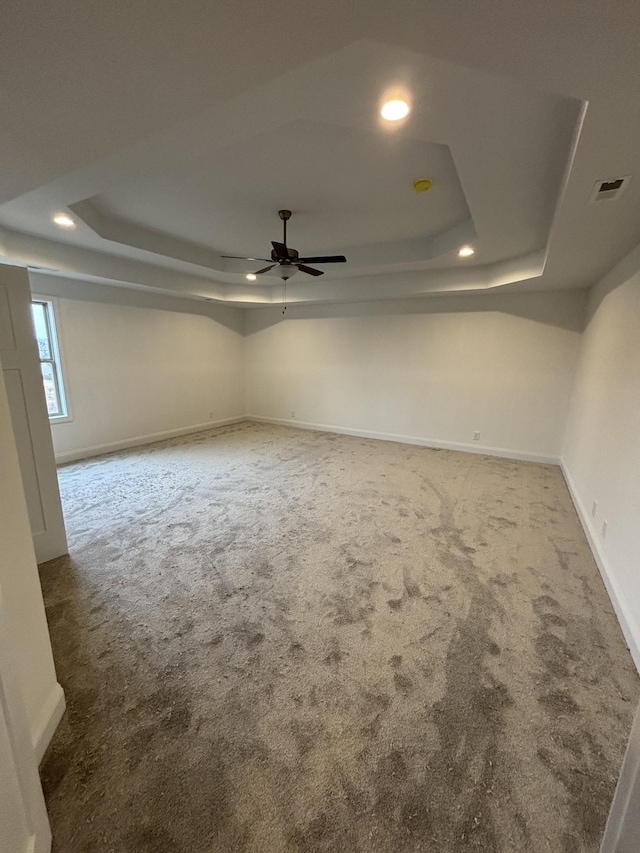 spare room featuring a tray ceiling, carpet flooring, visible vents, and ceiling fan