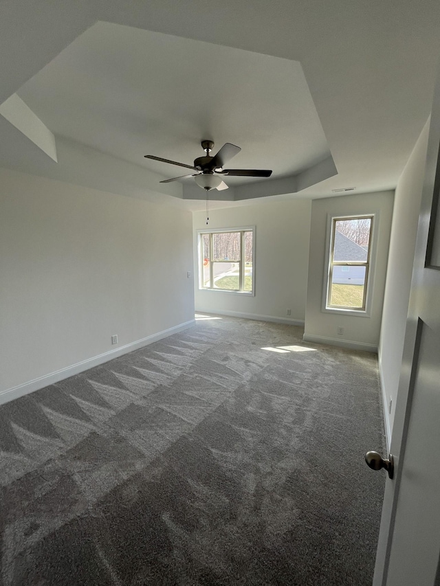 carpeted empty room featuring a wealth of natural light, baseboards, a raised ceiling, and ceiling fan