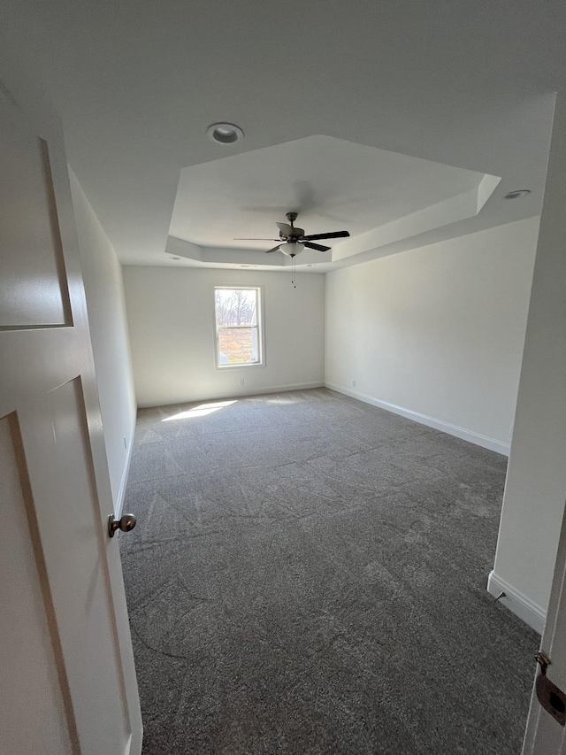 carpeted spare room with baseboards, a raised ceiling, and ceiling fan