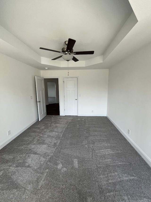 unfurnished bedroom with dark colored carpet, baseboards, a raised ceiling, and ceiling fan