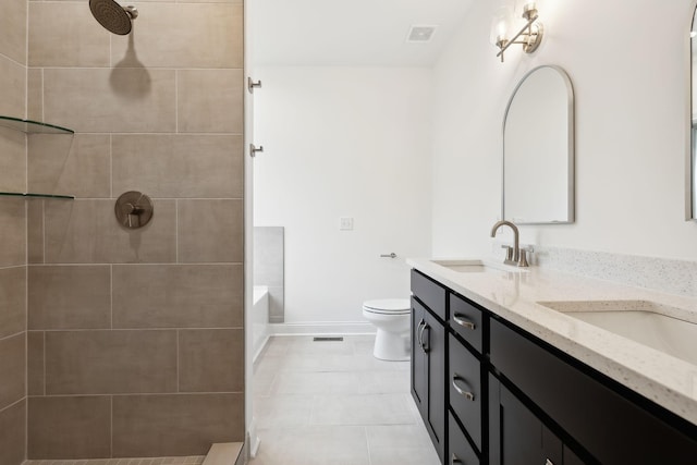 bathroom featuring toilet, tiled shower, a sink, baseboards, and double vanity