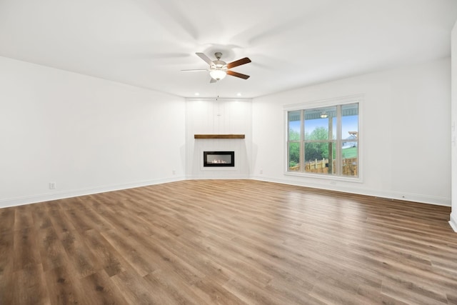 unfurnished living room featuring baseboards, wood finished floors, ceiling fan, and a glass covered fireplace