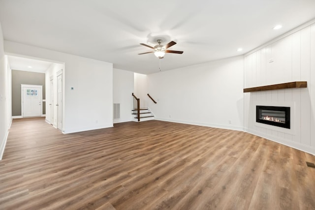 unfurnished living room featuring a fireplace, wood finished floors, ceiling fan, and stairway