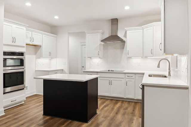 kitchen featuring dark wood finished floors, wall chimney exhaust hood, a sink, and stainless steel double oven