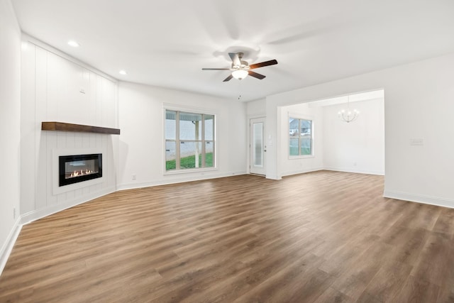 unfurnished living room with a large fireplace, baseboards, wood finished floors, recessed lighting, and ceiling fan with notable chandelier
