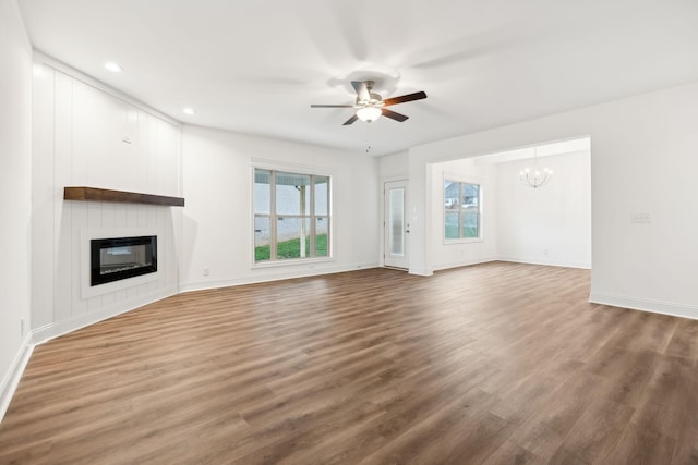 unfurnished living room with wood finished floors, a large fireplace, baseboards, ceiling fan with notable chandelier, and recessed lighting