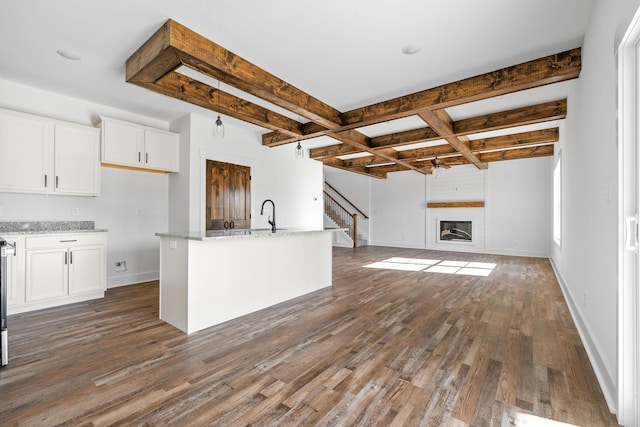 kitchen with white cabinetry, light stone countertops, dark hardwood / wood-style flooring, a fireplace, and a center island with sink