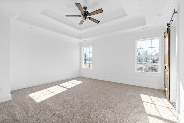 carpeted spare room with ceiling fan, a barn door, crown molding, and a tray ceiling