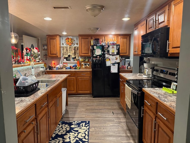 kitchen featuring visible vents, brown cabinetry, light wood-style flooring, black appliances, and a sink