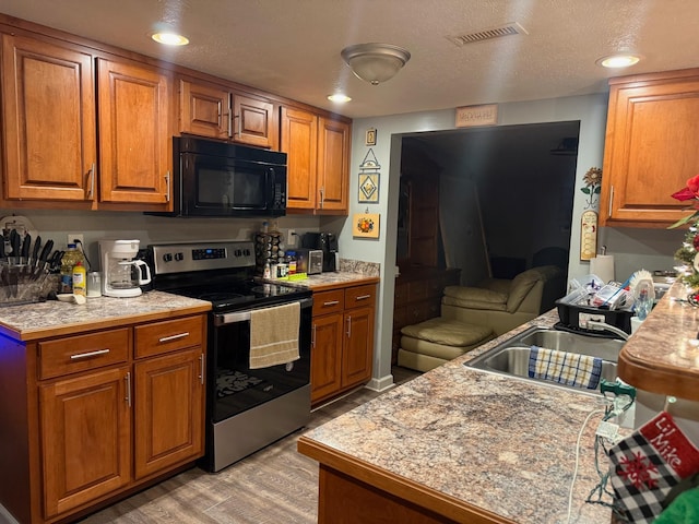 kitchen with a textured ceiling, sink, stainless steel range with electric stovetop, and light wood-type flooring