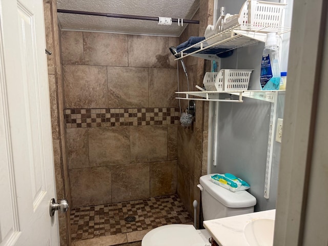 bathroom with tiled shower, toilet, a textured ceiling, and vanity