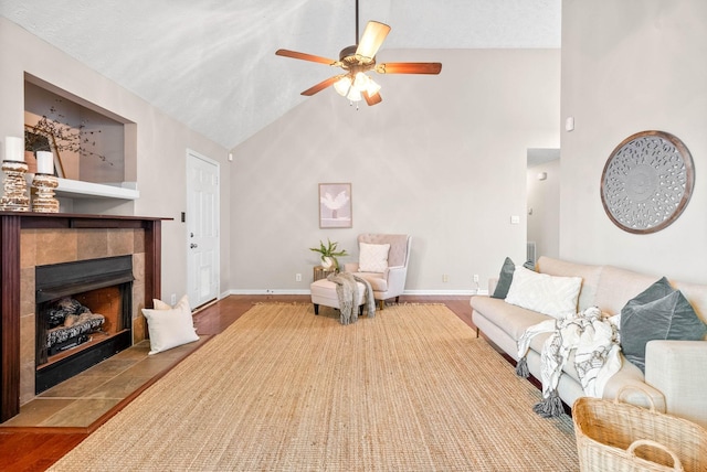 living room with a tiled fireplace, ceiling fan, and high vaulted ceiling