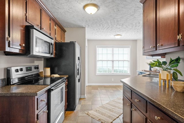 kitchen featuring light tile patterned floors, a textured ceiling, and appliances with stainless steel finishes