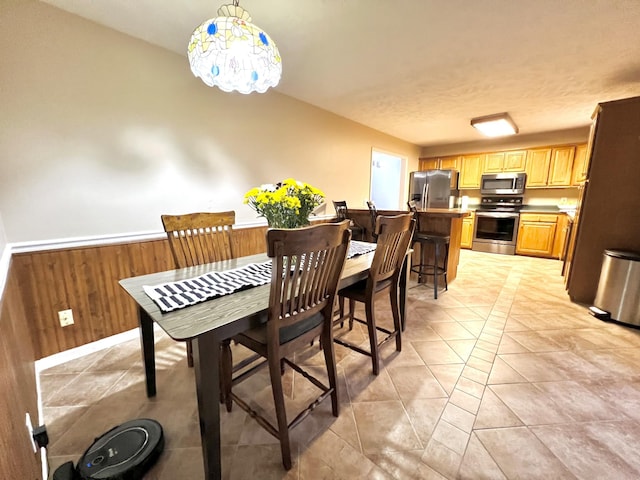 dining space featuring light tile patterned flooring, a textured ceiling, and wood walls