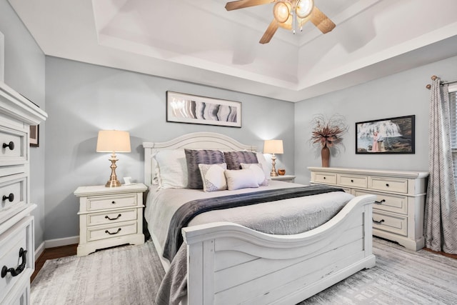 bedroom featuring ceiling fan, light wood-type flooring, and a tray ceiling