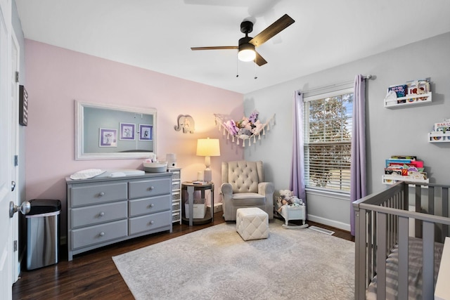 bedroom featuring dark hardwood / wood-style floors, ceiling fan, and a crib