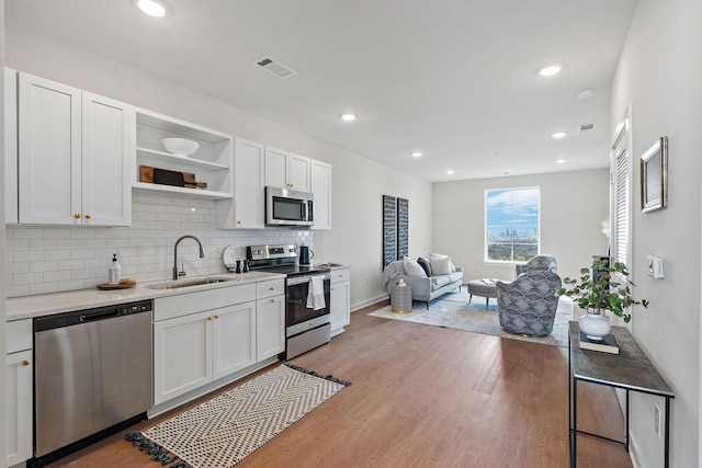 kitchen featuring backsplash, stainless steel appliances, sink, white cabinets, and light hardwood / wood-style floors