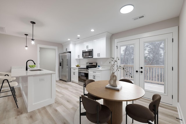 kitchen with light stone counters, stainless steel appliances, a center island with sink, white cabinets, and hanging light fixtures