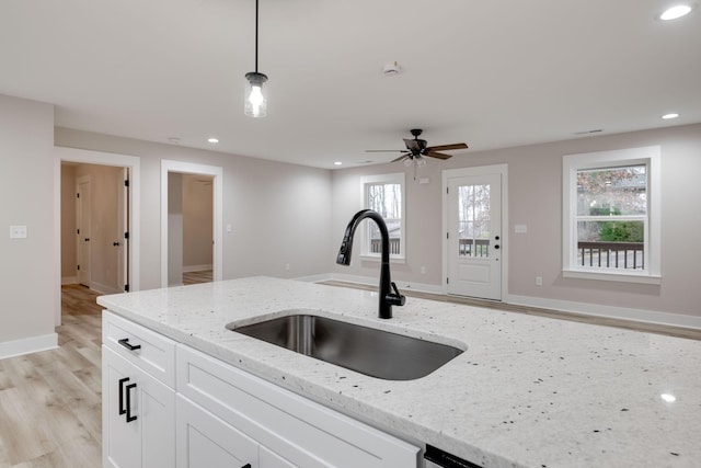 kitchen featuring pendant lighting, white cabinets, sink, light stone countertops, and light wood-type flooring