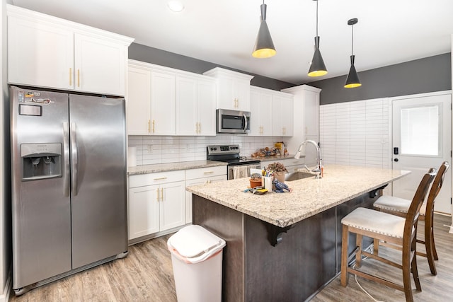 kitchen featuring appliances with stainless steel finishes, decorative light fixtures, white cabinetry, and a kitchen island with sink