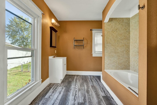 bathroom with a tub to relax in, vanity, a healthy amount of sunlight, and hardwood / wood-style flooring