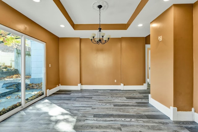 empty room featuring a tray ceiling, hardwood / wood-style floors, and a notable chandelier