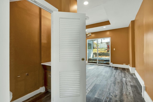 hall with dark wood-type flooring, a tray ceiling, and an inviting chandelier