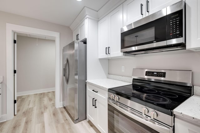 kitchen with light stone countertops, appliances with stainless steel finishes, white cabinets, and light hardwood / wood-style flooring