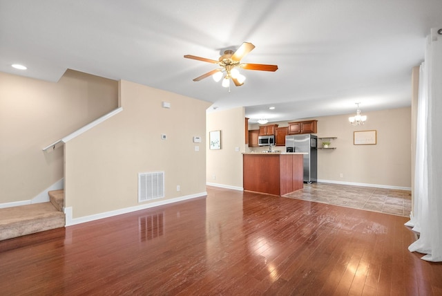 unfurnished living room with ceiling fan with notable chandelier and dark hardwood / wood-style flooring