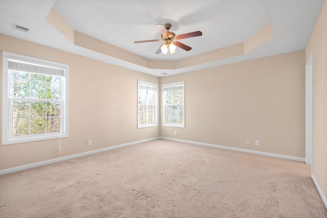 empty room featuring ceiling fan, a raised ceiling, and light carpet