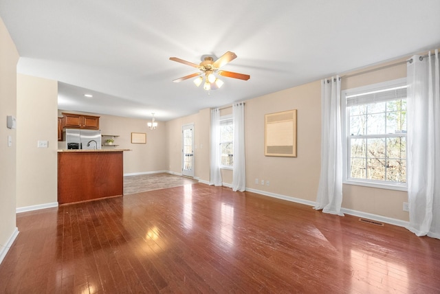 unfurnished living room with ceiling fan with notable chandelier and dark hardwood / wood-style flooring