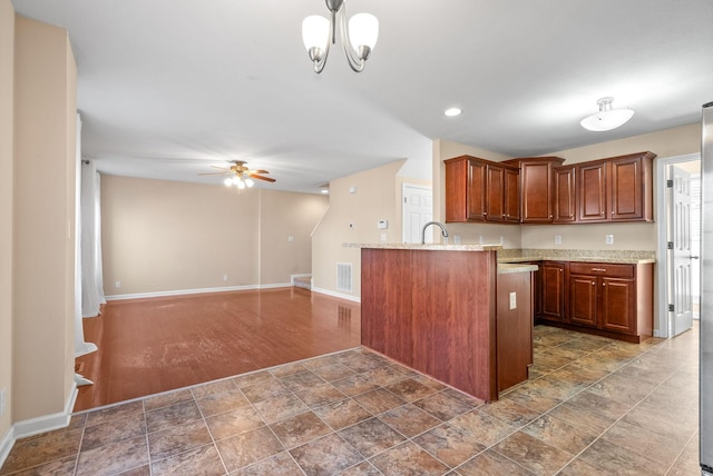 kitchen featuring pendant lighting, ceiling fan with notable chandelier, sink, light stone counters, and kitchen peninsula