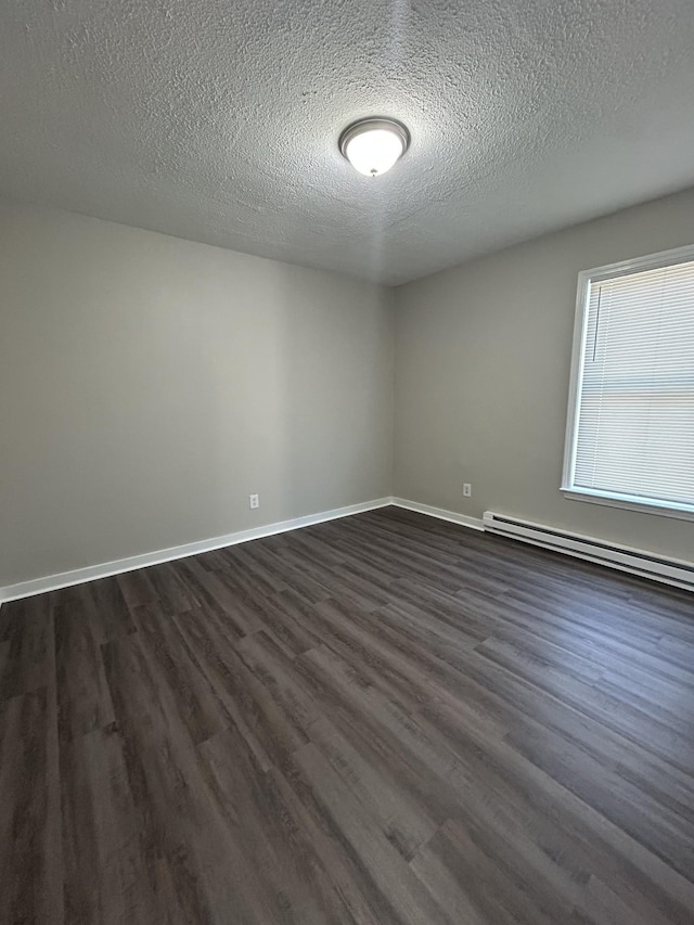 spare room featuring baseboard heating, dark wood-type flooring, and a textured ceiling