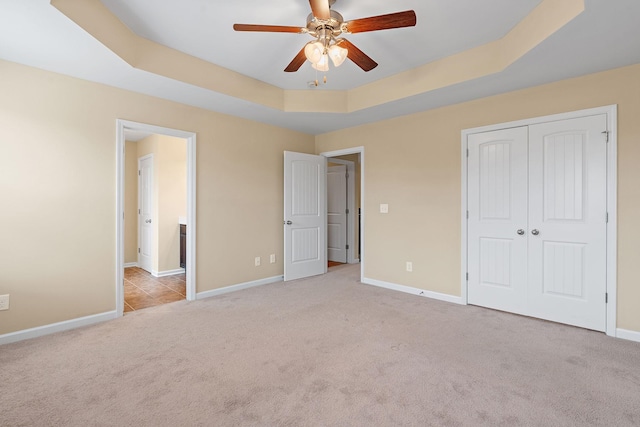 unfurnished bedroom featuring ceiling fan, light colored carpet, and a tray ceiling