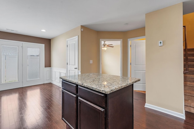 kitchen with a center island, ceiling fan, light stone counters, dark hardwood / wood-style flooring, and dark brown cabinetry